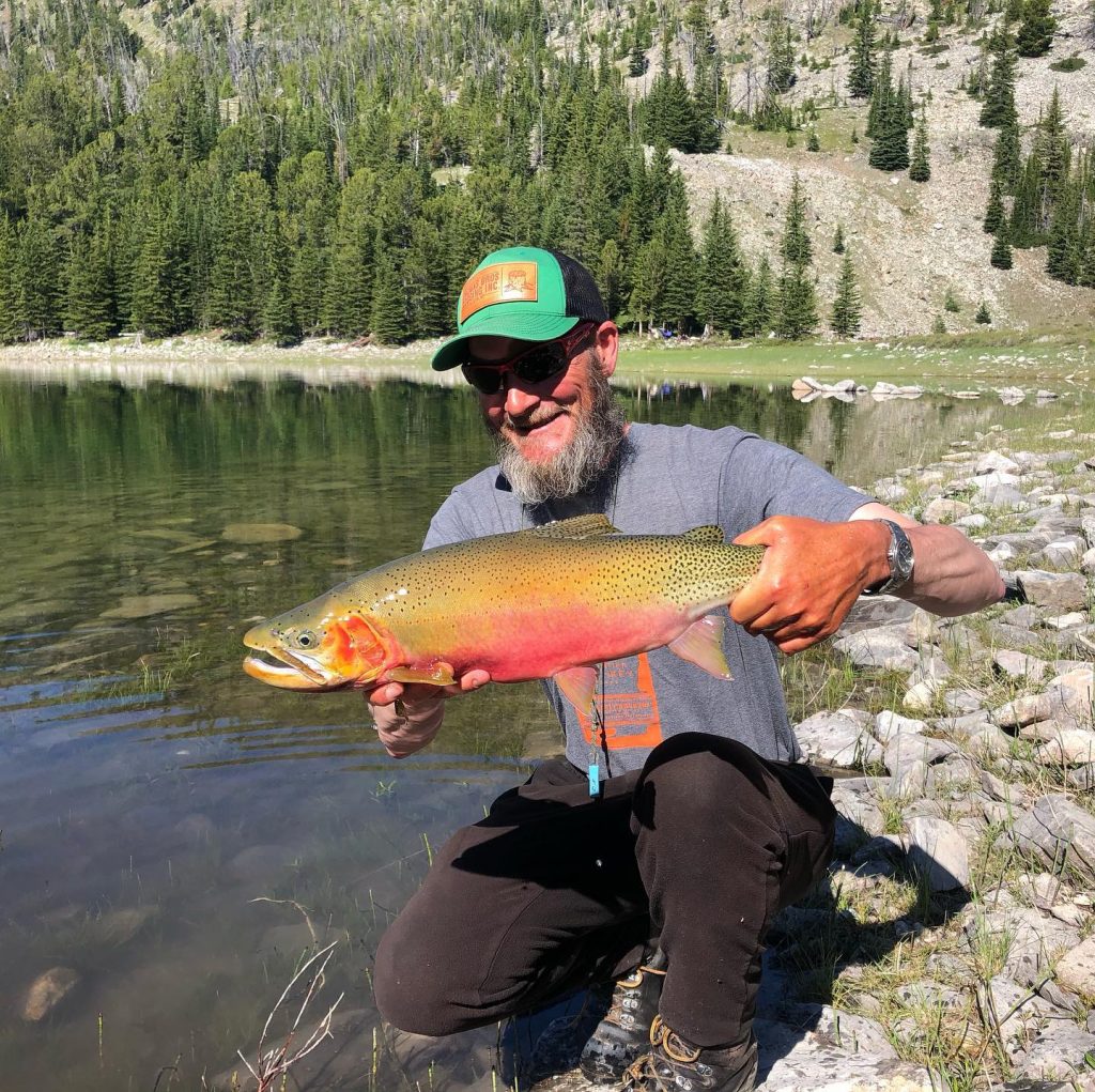 Man kneeling by river holding a huge trout he just caught
